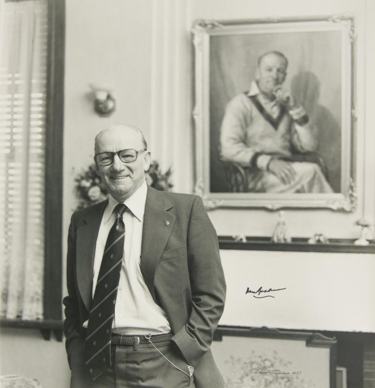 Item #32783 A masterly 1977 portrait by the Adelaide photographer David Simpson, featuring a distinguished but relaxed Sir Don at home, standing in front of his familiar portrait in oils. Cricket, Sir Donald BRADMAN.